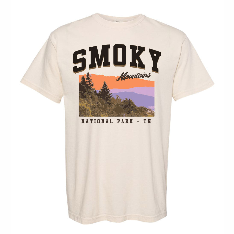 The Smoky Mountains Graphic Tee features a colorful mountain sunset above the trees in the Smoky Mountains National Park, printed on an off-white t-shirt. Sold by The DW Designs, Knoxville, TN.