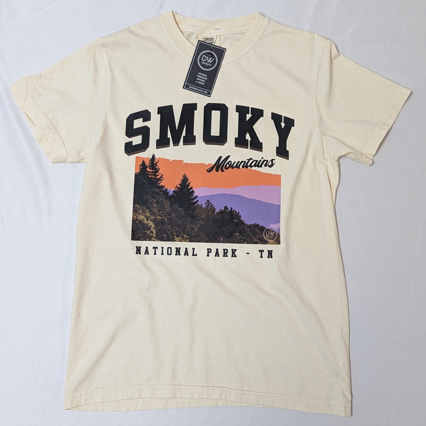 The Smoky Mountains Graphic Tee features a colorful mountain sunset above the trees in the Smoky Mountains National Park, printed on an off-white t-shirt. Sold by The DW Designs, Knoxville, TN.